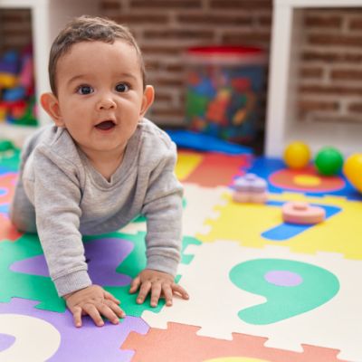 A baby is crawling on a colorful foam puzzle mat in a playroom setting.