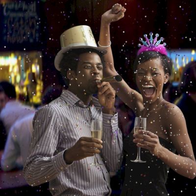 A festive celebration with two people cheering, wearing party hats, and holding drinks, surrounded by a lively atmosphere and confetti.