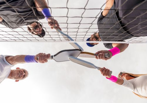 Four people near a tennis net holding badminton rackets towards the center, wearing colorful wristbands.