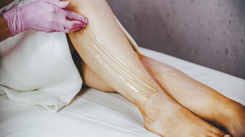 A person is applying a wax-like substance to their leg while wearing pink gloves, possibly preparing for hair removal.