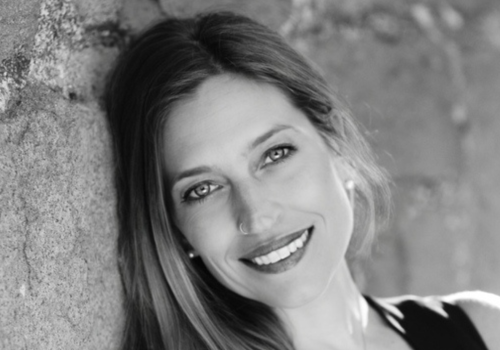 A black and white photo of a woman smiling, leaning against a wall.