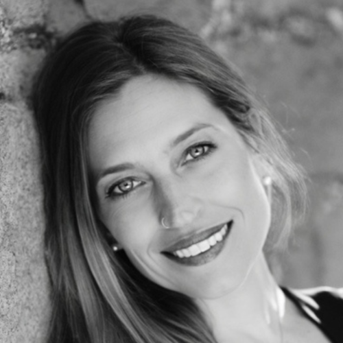 A black and white photo of a woman smiling, leaning against a wall.