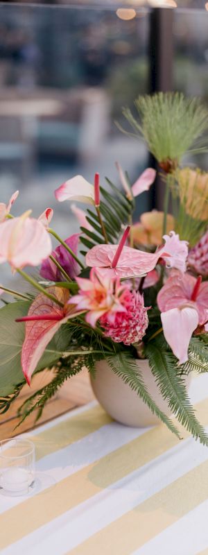 A vibrant flower arrangement in a white vase with pink and green foliage on a table with a striped cloth.