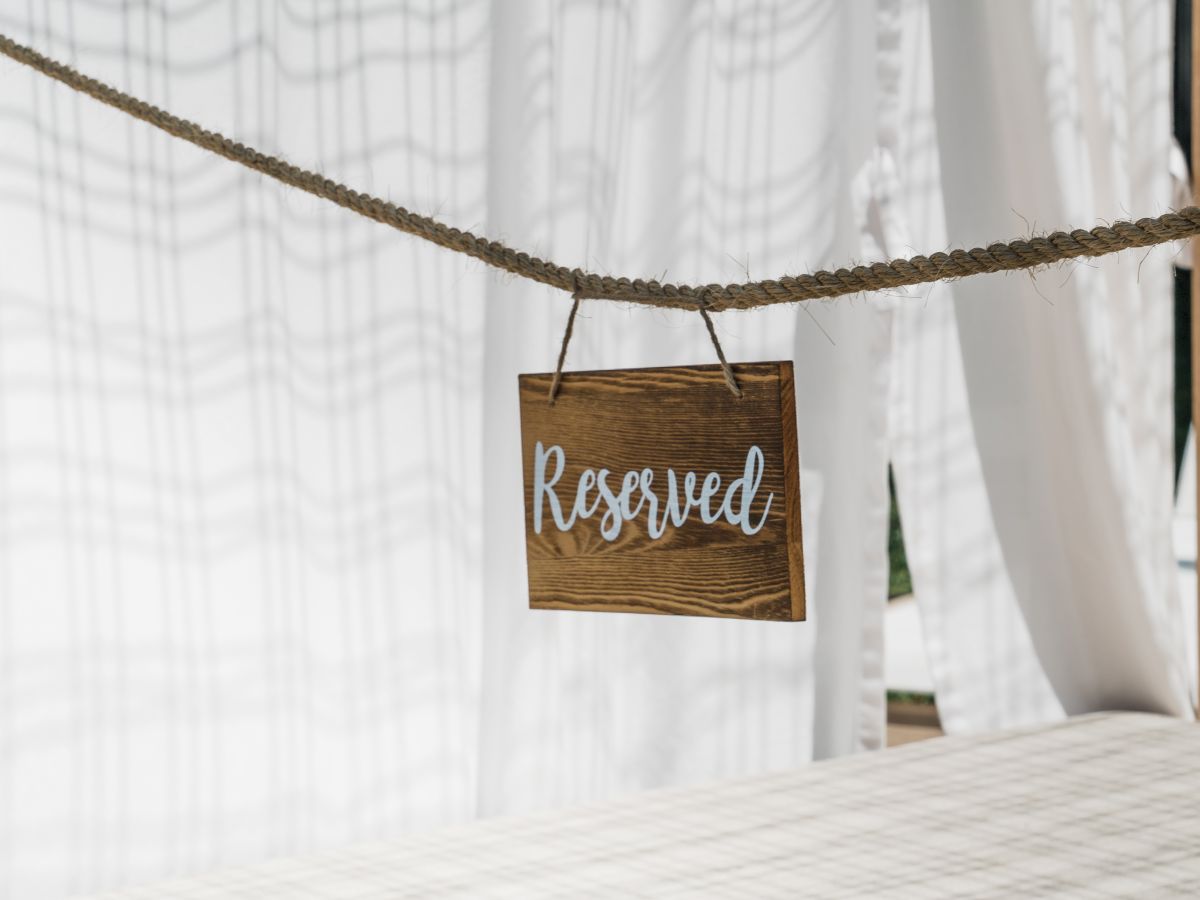 A wooden sign saying "Reserved" hangs on a rope, with sheer white curtains in the background.