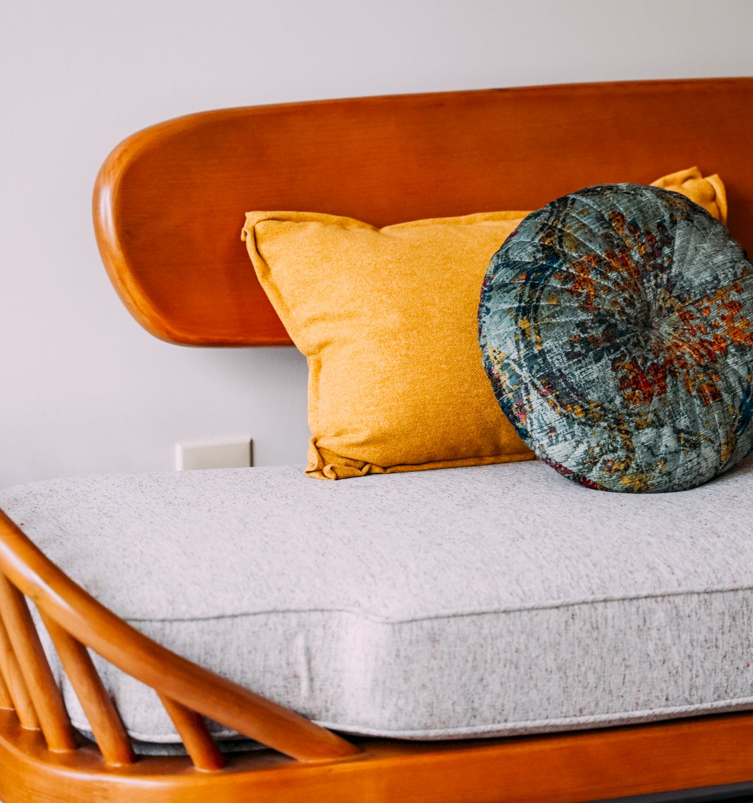 A wooden-backed couch with two yellow pillows and a round, patterned cushion placed on a light-colored seat cushion.